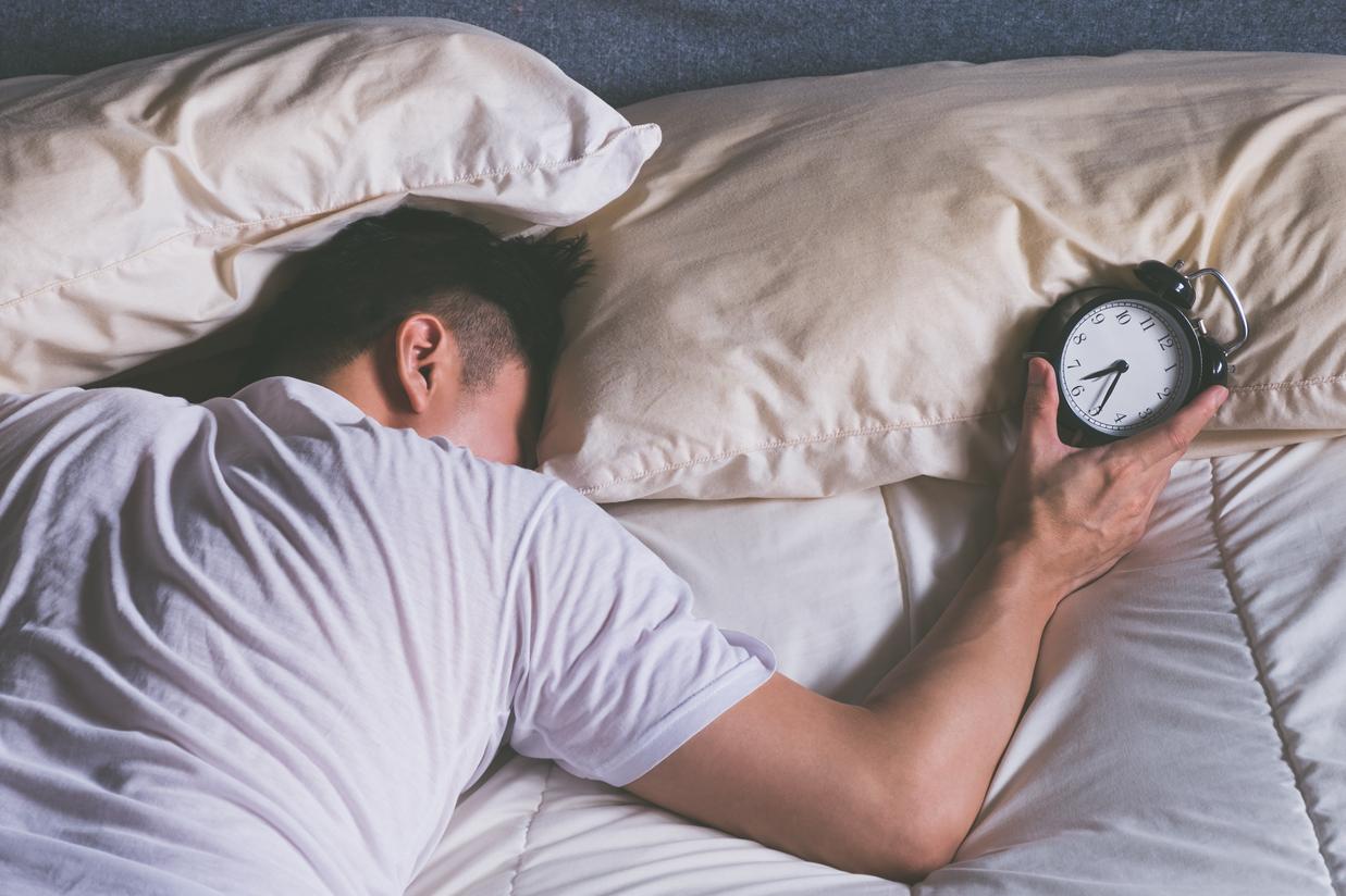 Homme allongée dans son lit, l'air fatigué, arrêtant son reveil